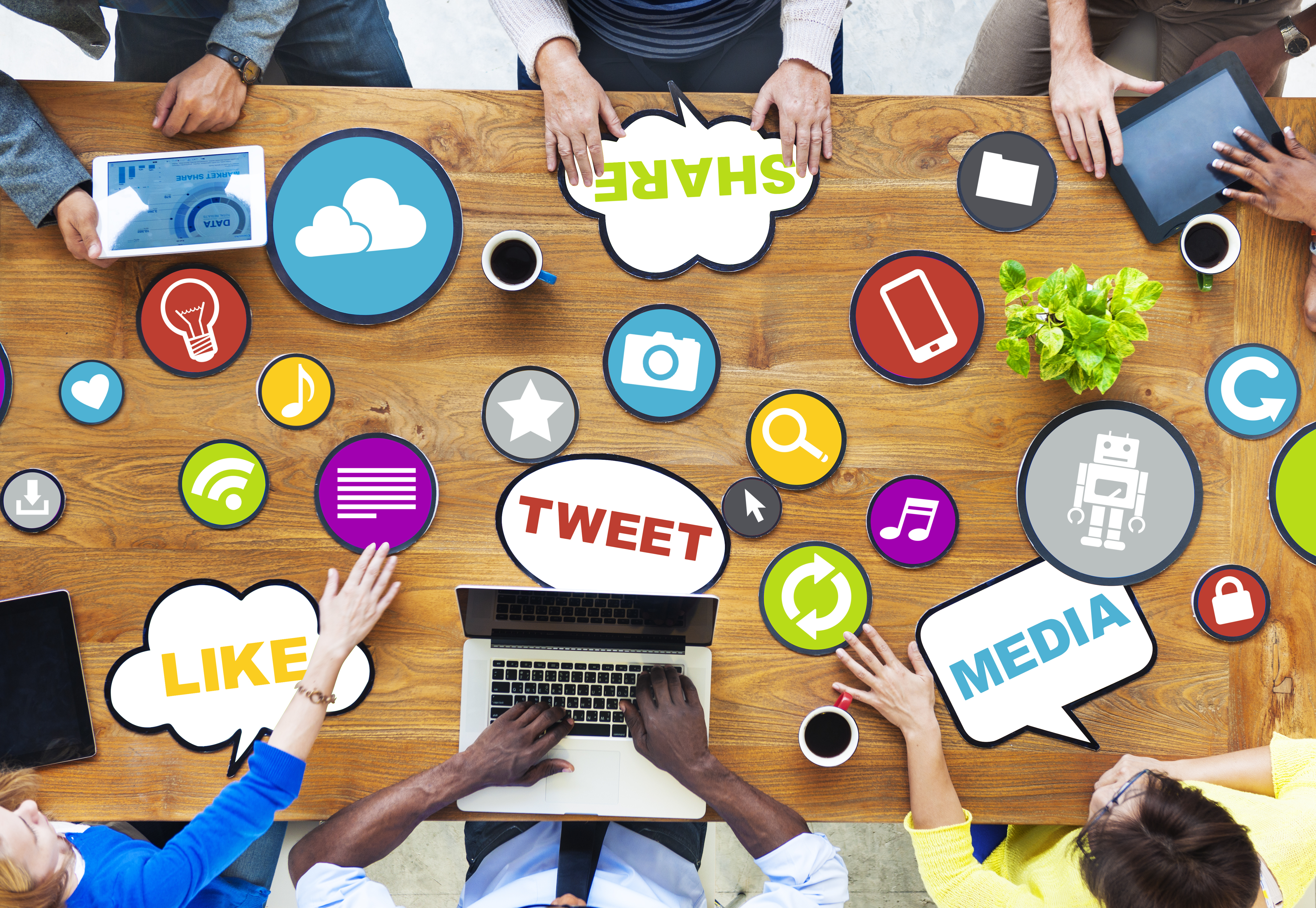 Image displays a group of people sitting around a table. On the table, various social media terms are laid in front of the group such as, 'tweet', 'media', 'like', etc.